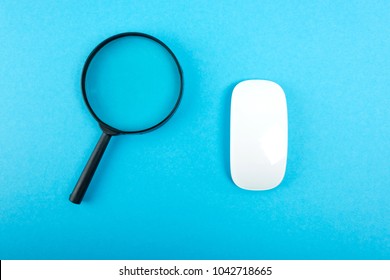 Magnifying Glass And White Pc Mouse On Blue Table. Top View.