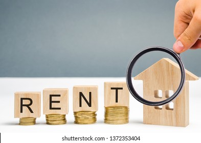 Magnifying Glass, Wooden Blocks With The Word Rent, Coins And A Miniature House. The Concept Of Renting Housing And Real Estate. The Cost Of A Rented Home Or Apartment. Saving Money. Rental.