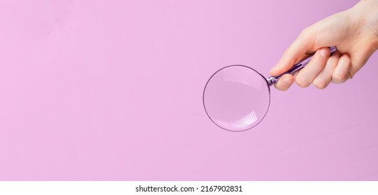 Magnifying lens in hand on pink ad banner with copy space for text. High quality photo