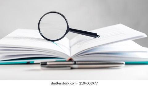 Magnifying lens over open paper book with pages. Concept of academic research. - Shutterstock ID 2104008977