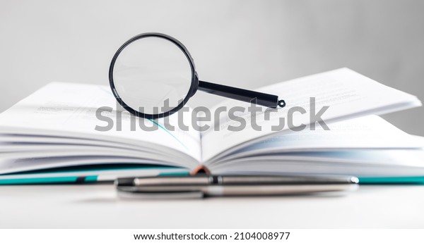 Magnifying lens over open paper book with\
pages. Concept of academic\
research.
