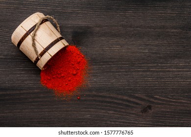 Magyar (Hungarian) brilliant red sweet paprika powder. Traditional seasoning for cooking national food. Wooden keg, black wooden background, copy space, top view