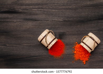 Magyar (Hungarian) brilliant red sweet and hot paprika powder. Traditional seasoning for cooking national food. Wooden kegs, black wooden background, copy space, top view