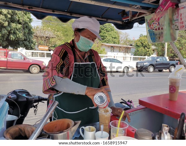Mahasarakham, Thailand -​ February, 25, 2020.The\
seller who wears a Corona anti-virus mask Intentionally making iced\
coffee behind the\
cart.