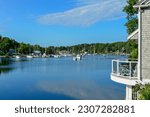 Mahone Bay, Nova Scotia, Canada-May 2023: A view of Mahone Bay with recreational vessels moored in the cove. A wooden house with cedar shakes and a small patio deck on the edge of the blue water.