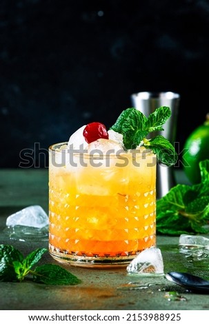 Mai Tai popular alcoholic cocktail with rum, liqueur, syrup, lime juice, mint and crushed ice. Dark green background, steel bar tools, negative space