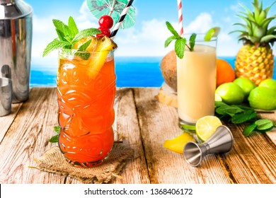 Mai Tai and Zombie tiki cocktails, with straw, umbrella, maraschino cherries and pineapple wedge, on a wooden table. Shaker and sea in the background.  - Powered by Shutterstock