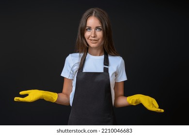 The Maid In A Black Apron And Yellow Gloves Does Not Know And Spread Her Hands To The Sides.