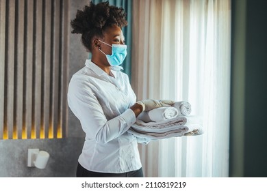 Maid With Face Protective Mask Cleaning A Hotel Room During Pandemic. Maid Working At A Hotel Wearing A Protective Face Mask And Bringing Fresh Clean Towels In The Room, During COVID-19