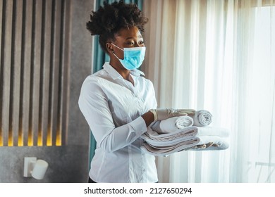 Maid With Face Protective Mask Cleaning A Hotel Room During Pandemic. Maid Working At A Hotel Wearing A Protective Face Mask And Bringing Fresh Clean Towels In The Room, During COVID-19