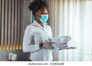 Maid With Face Protective Mask Cleaning A Hotel Room During Pandemic. Maid Working At A Hotel Wearing A Protective Face Mask And Bringing Fresh Clean Towels In The Room, During COVID-19