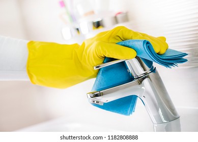 Maid hand or charwoman cleaning modern new basin in bathroom, water tap clean using yellow gloves and blue cloth.