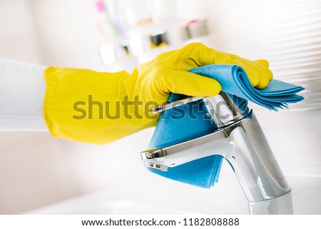 Maid hand or charwoman cleaning modern new basin in bathroom, water tap clean using yellow gloves and blue cloth.