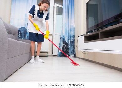 Maid Or Housekeeper In A Neat White Apron Cleaning A Living Room Floor With A Colorful Red Mop, Low Angle View At Floor Level