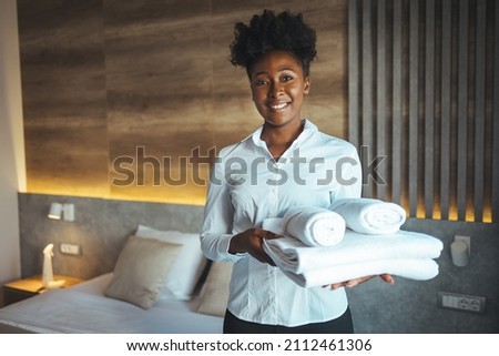 Maid putting stack of fresh white bath towels on the bed sheet. Room service maid cleaning hotel room. Maid making bed in hotel room. Change of towels in the hotel room