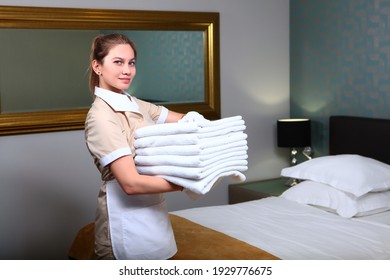 Maid In White Cotton Gloves Holds A Stack Of Towels. Friendly Hotel Staff. The Concept Of The Hotel Business. Photos In The Interior.