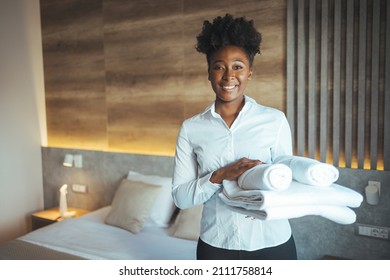 Maid working at a hotel holding towels and looking at the camera smiling - housekeeping concepts. Maid with fresh clean towels during housekeeping in a hotel room