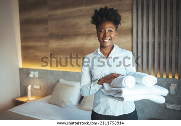 Maid working at a hotel\
holding towels and looking at the camera smiling - housekeeping\
concepts. Maid with fresh clean towels during housekeeping in a\
hotel room