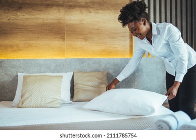 Maid working at a hotel making the bed and pillows. Maid making bed in hotel room. Housekeeper Making Bed. Young maid making bed in light hotel room.