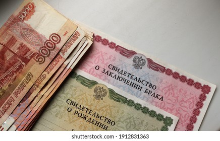 Maikop, Adygea Republic, Russia - February 6, 2021: Russian Supporting Documents Of A Child's Birth And Marriage Certificate Coupled With A Large Amount Of Cash On A White Background With Copy Space