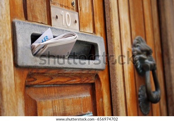 Mail box filled with rolled spam newspaper in old\
wooden door