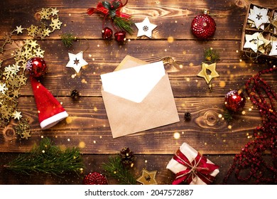 Mail envelope made of craft paper with a white sheet for text on a wooden background with Christmas decor. A letter to Santa Claus, a wish list, a new year's dream, a gift. Flat lay, copy space