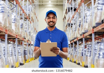 mail service and shipment concept - happy indian delivery man or warehouse worker with clipboard in blue uniform over goods background - Powered by Shutterstock