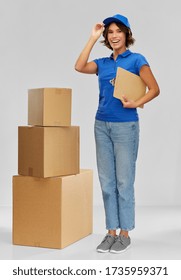 Mail Service And Shipment Concept - Happy Smiling Delivery Girl In Blue Uniform With Parcel Boxes And Clipboard Over Grey Background