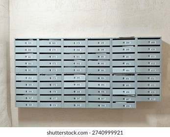 Mailboxes are mounted on a wall. Each box has a number and is used for receiving mail. The setting is indoors during the day.