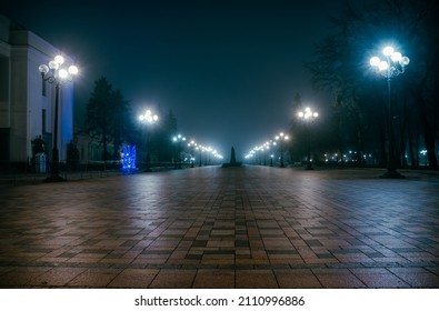 The main alley of a night early winter park in a light fog. Footpath in a fabulous late autumn city park at night with benches and latterns. Beautiful cold evening in Mariinsky Park. Kyiv, Ukraine. - Shutterstock ID 2110996886