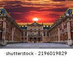 The main entrance to the Palace of Versailles just outside Paris, France is seen under a colourful red and orange sunset.