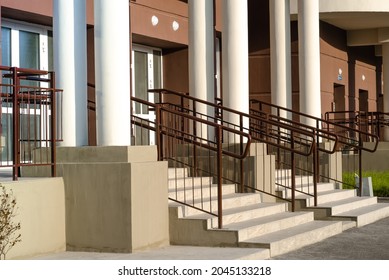main entrance with stairs and railings of  residential apartment building with brown walls and white columns. Construction of new housing.