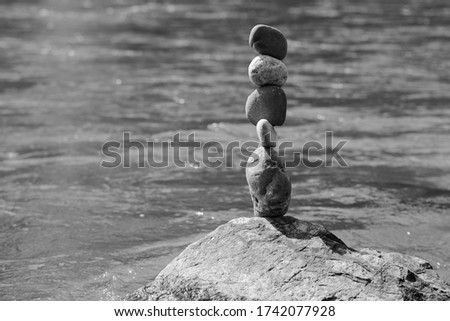 The Main focus of Five, Large, Heavy pebbles of varying sizes balanced vertically on top of each other, on a even larger boulder by the side of a slightly out of focus fast moving river. 2020