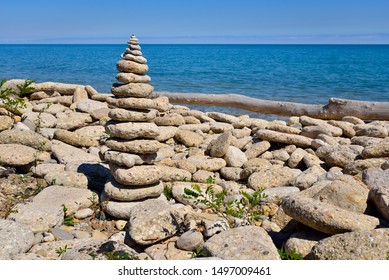 The main focus is on the stack of progressively smaller and smaller rocks and stones.  The pile is along the shore of Lake Michigan with the aqua blue waterscape beyond.  