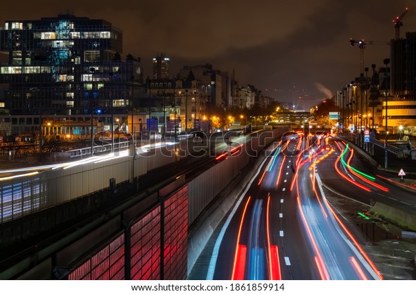 Main highway with many lanes in suburbian La\
Defense Paris leading into the city centre of the french capital\
metropole with light traces of cars and metro train, illuminated\
buildings at night.