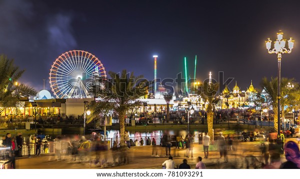 Main square and lake in Global Village with crowd\
and attractions timelapse in Dubai, UAE. Brightly colouredl lights\
and highly detailed pavilion facades have helped make Global\
Village one of Dubai\'s