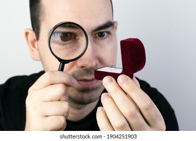 The main subject is out of focus, man hold magnifying glass closeup look at ring box, expensive or cheap wedding,  fake diamond problem