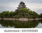 The main tower of Hiroshima Castle (Carp Castle) on the shore of a defensive moat on an autumn day, Hiroshima, Japan