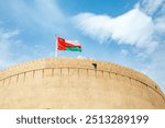 Main tower of Nizwa arabic citadel fortress with Omani flag waving on top, Nizwa, sultanate Oman