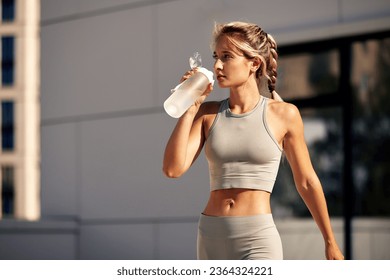 Maintaining hydration. A woman drinks water during a workout, replenishing her water-salt balance, beautiful light, a woman quenches her thirst on a sunny day