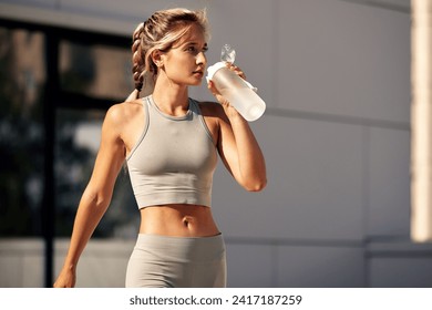 Maintaining hydration. A woman drinks water during a workout, replenishing her water-salt balance, beautiful light, a woman quenches her thirst on a sunny day - Powered by Shutterstock