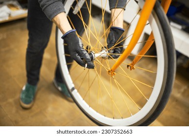 Maintenance of a bicycle: hands of an unrecognizable man using gloves disassembling the front wheel of an orange bike in his repair shop. - Powered by Shutterstock