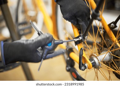 Maintenance of a bicycle: hands of an unrecognizable person using gloves disassembling an orange bike with a hex allen key in his repair shop. Selective focus composition. - Powered by Shutterstock