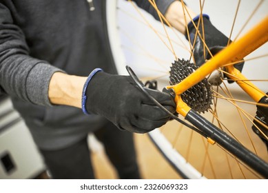 Maintenance of a bicycle: hands of an unrecognizable person using gloves disassembling the rear wheel of an orange bike in his repair shop. - Powered by Shutterstock