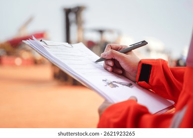 Un ingeniero de mantenimiento está verificando la lista de verificación para verificar la condición de la carretilla elevadora o el vehículo pesado de la máquina, con el fondo del lugar de trabajo del sitio de construcción. Escena de trabajo del Industrial, primer plano.