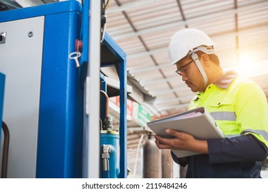 A Maintenance Engineer Wearing Green Protective Clothing Uses Laptops And Tablets To Inspect Factory Electrical Systems.