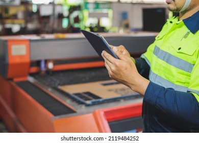 A Maintenance Engineer Wearing Green Protective Clothing Uses Laptops And Tablets To Inspect Factory Electrical Systems.