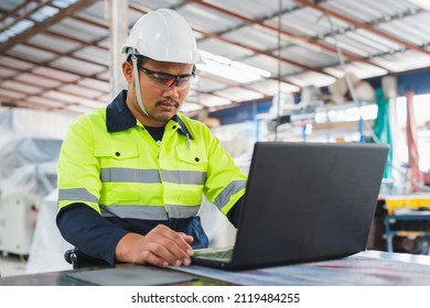 A Maintenance Engineer Wearing Green Protective Clothing Uses Laptops And Tablets To Inspect Factory Electrical Systems.