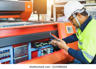 A Maintenance Engineer Wearing Green Protective Clothing Uses Laptops And Tablets To Inspect Factory Electrical Systems.