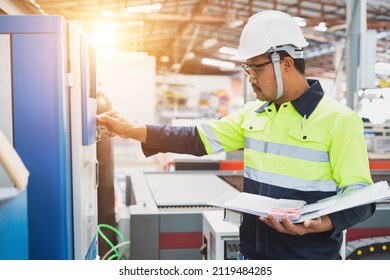 A Maintenance Engineer Wearing Green Protective Clothing Uses Laptops And Tablets To Inspect Factory Electrical Systems.